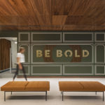 Modern Detroit office lobby with green wainscoting, BE BOLD wall text, wood ceiling and leather benches